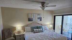 Ein Schlafzimmer mit Bett, Nachttisch, Stuhl, Deckenventilator und Blick auf den Außenbalkon.