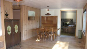 Una habitación amplia con suelo de madera, una mesa de comedor con sillas, un mueble de madera y una lámpara colgante.