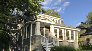 Une maison à deux étages, avec des fondations en pierre, des éléments décoratifs blancs et un porche doté d’un escalier.