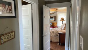 Un couloir menant à une chambre à coucher équipée d’un lit, d’une table de chevet et d’une lampe.