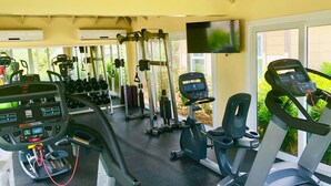 A gym with cardio machines, weightlifting equipment, and a TV screen.