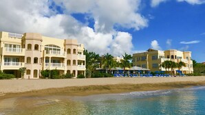 A beachfront hotel with multiple balconies, a pool area with umbrellas, and palm trees.