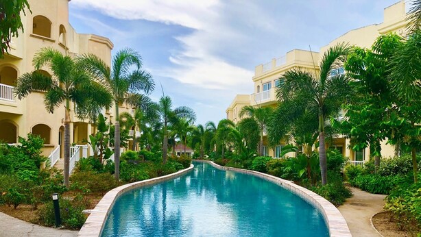 A swimming pool surrounded by palm trees and buildings with balconies.