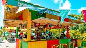 A colorful outdoor bar with a wooden deck, featuring a counter with stools and various signs.