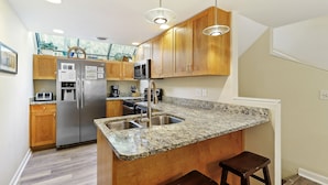 Una cocina moderna con encimeras de granito, electrodomésticos de acero inoxidable, armarios de madera e iluminación colgante.