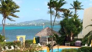 A pool area with lounge chairs and a small gazebo, surrounded by palm trees and a view of the sea. - Beachfront Caribbean Paradise at Colony Cove (Christiansted)