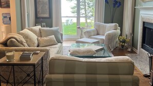 A living room with a large window, a fireplace, and a view of the outdoors. - Beautiful Lake Charlevoix Sandy Beach- Best North Shore Location (Boyne City)