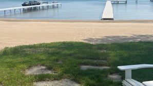 A beach with a wooden pier extending into calm waters, a white bench, and a small dock with a boat. - Beautiful Lake Charlevoix Sandy Beach- Best North Shore Location (Boyne City)