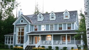 A two-story house with a front porch, large windows, and a chimney. - Beautiful Lake Charlevoix Sandy Beach- Best North Shore Location (Boyne City)