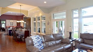 A spacious living room with a leather sofa, a dining area with a kitchen in the background, large windows, and a star decoration on the wall.