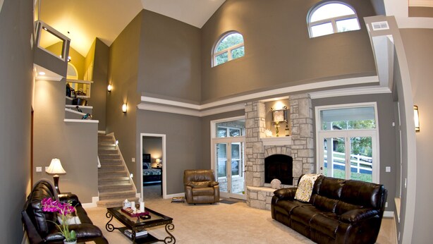 A spacious living room with a fireplace, leather furniture, a staircase, and large windows.