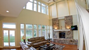 A spacious living room with a stone fireplace, leather sofa, and large windows offering a view of the outdoors.