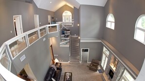 A spacious loft with a high ceiling, a fireplace, a staircase, and a balcony.