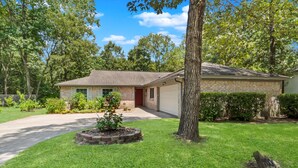 Une maison de plain-pied avec un garage à l’avant, entourée d’une pelouse bien entretenue et d’arbres.