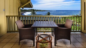 Ein Balkon mit Blick auf das Meer, zwei Korbstühle und ein Holztisch.