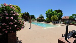 A pool area with a clear blue sky, a brick planter with pink flowers, and lounge chairs.