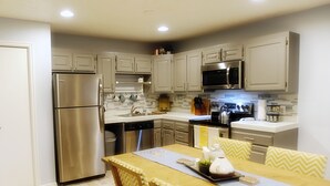 A modern kitchen with stainless steel appliances, a dining table with chairs, and a tiled backsplash.