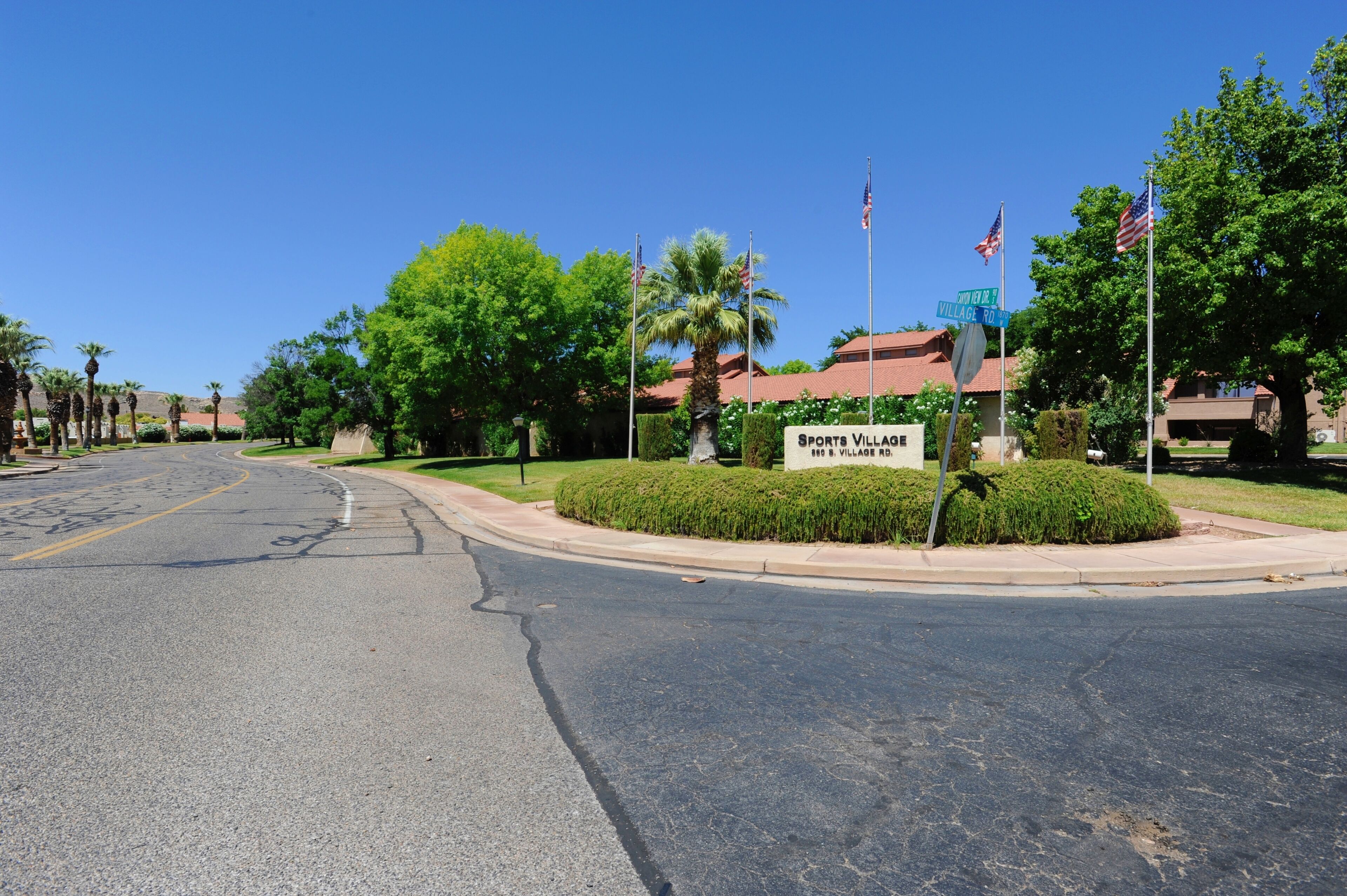 A street view with a sign for Sports Village Rd. There are palm trees and a building with a red roof.