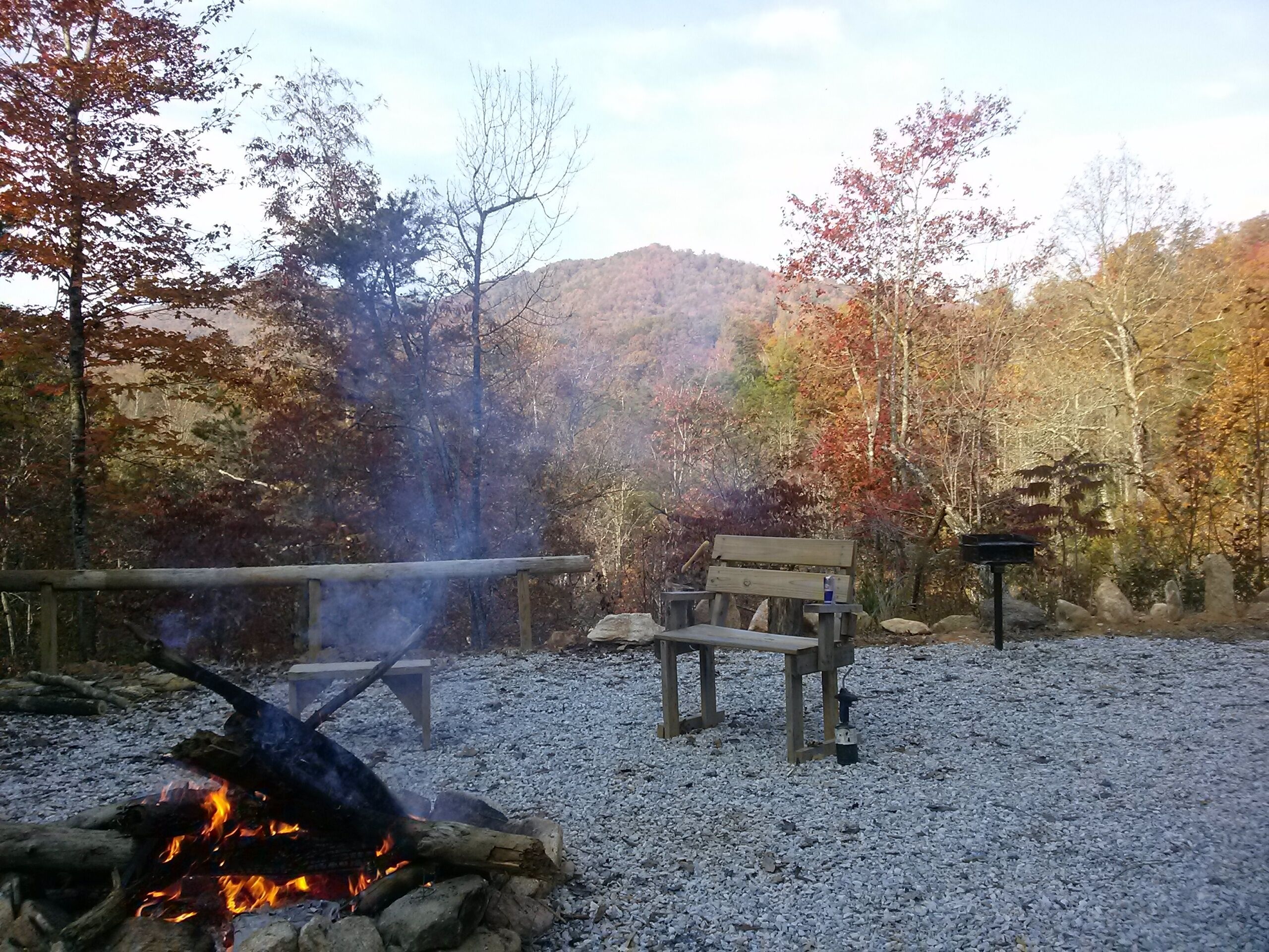 A campsite with a fire pit, a bench, and a picnic table surrounded by gravel.