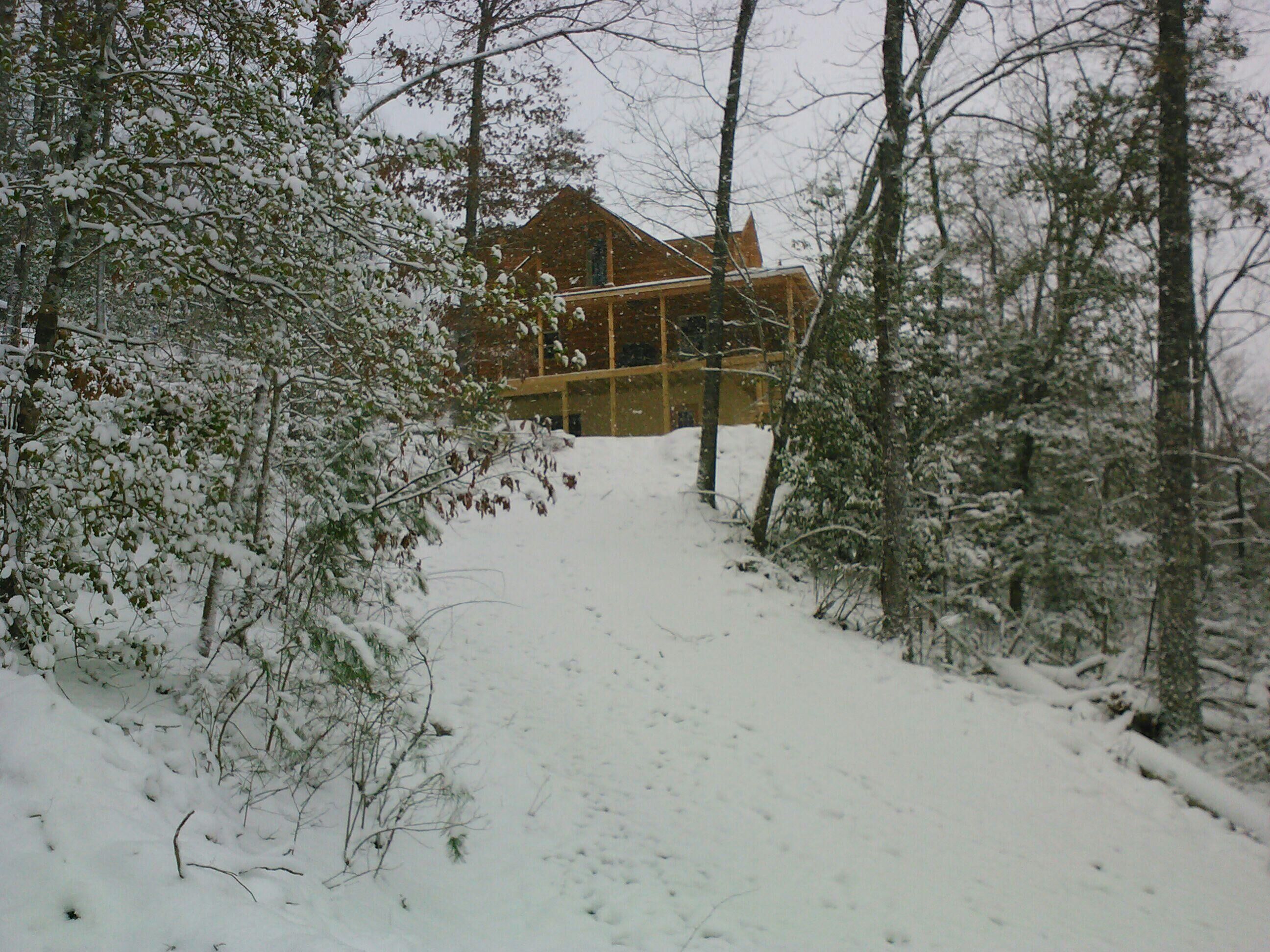 Une cabane au cœur d’une forêt enneigée, dotée d’une terrasse en bois visible et d’une grande fenêtre.