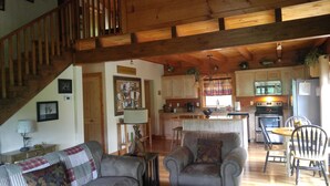 A cozy living room with a sofa, a coffee table, and a dining area with chairs. A kitchen with wooden cabinets and appliances is visible in the background. -  Secluded Mountainside Cabin, Close to Town, No 4 wheel drive needed!  Hot Tub! (Bryson City)