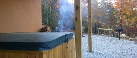 A wooden hot tub with a black cover, surrounded by a gravel area and wooden structures.