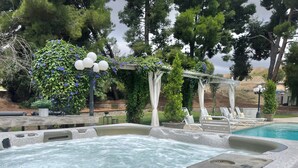 A hot tub area with a pool, lounge chairs, and a pergola with climbing plants.