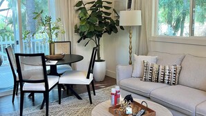 A modern living room with a round coffee table, a sofa, a dining table with chairs, and a large potted plant.