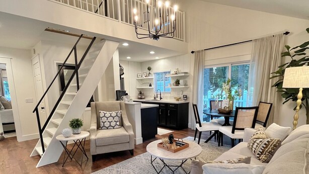 A spacious living room with a high ceiling, a staircase, a kitchen area, and a dining setup.