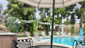 A poolside area with a round metal table, lounge chairs, and a pergola with climbing plants.