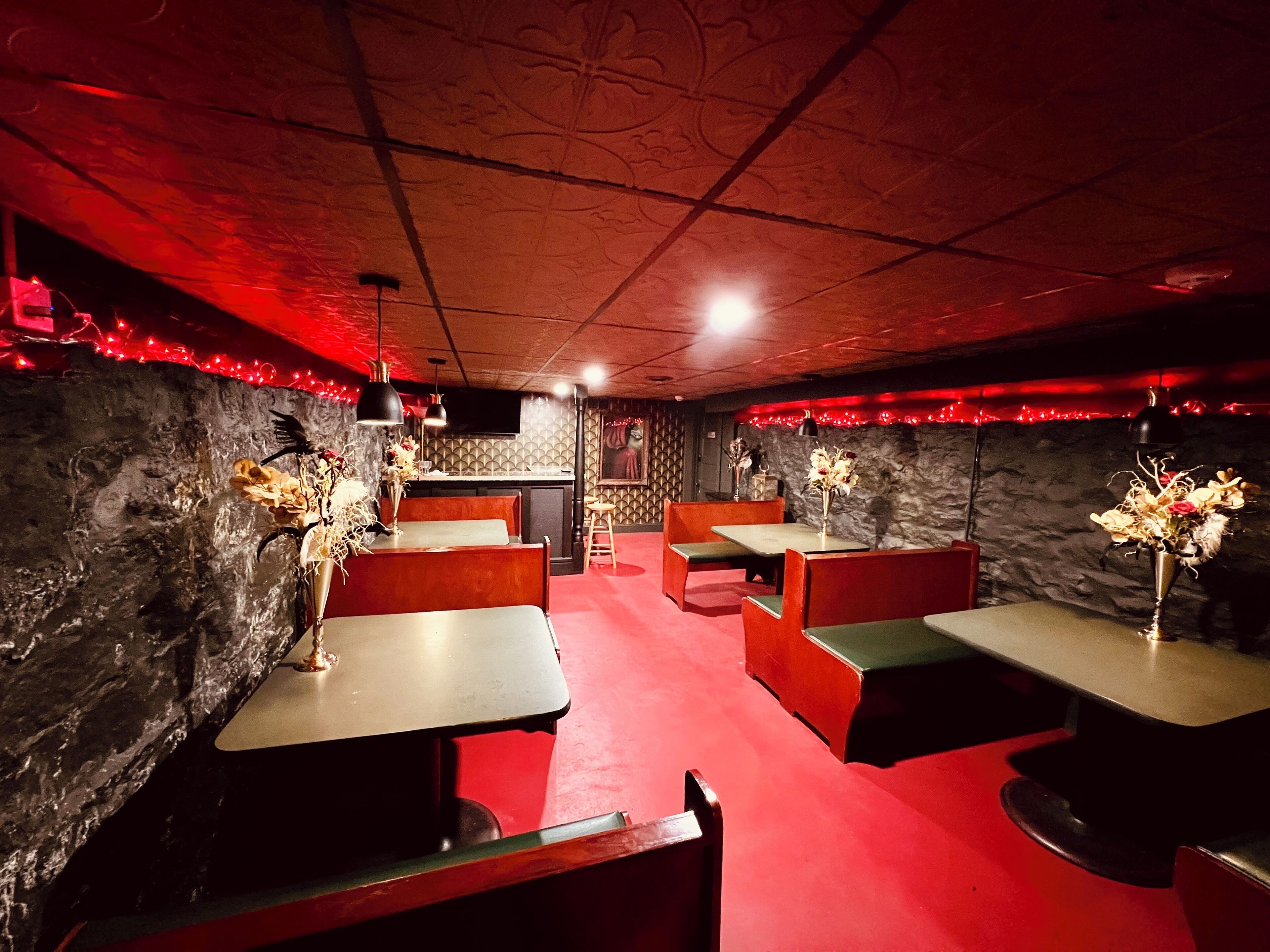 A dimly lit restaurant with booths and tables, red carpet flooring, and decorative lighting.