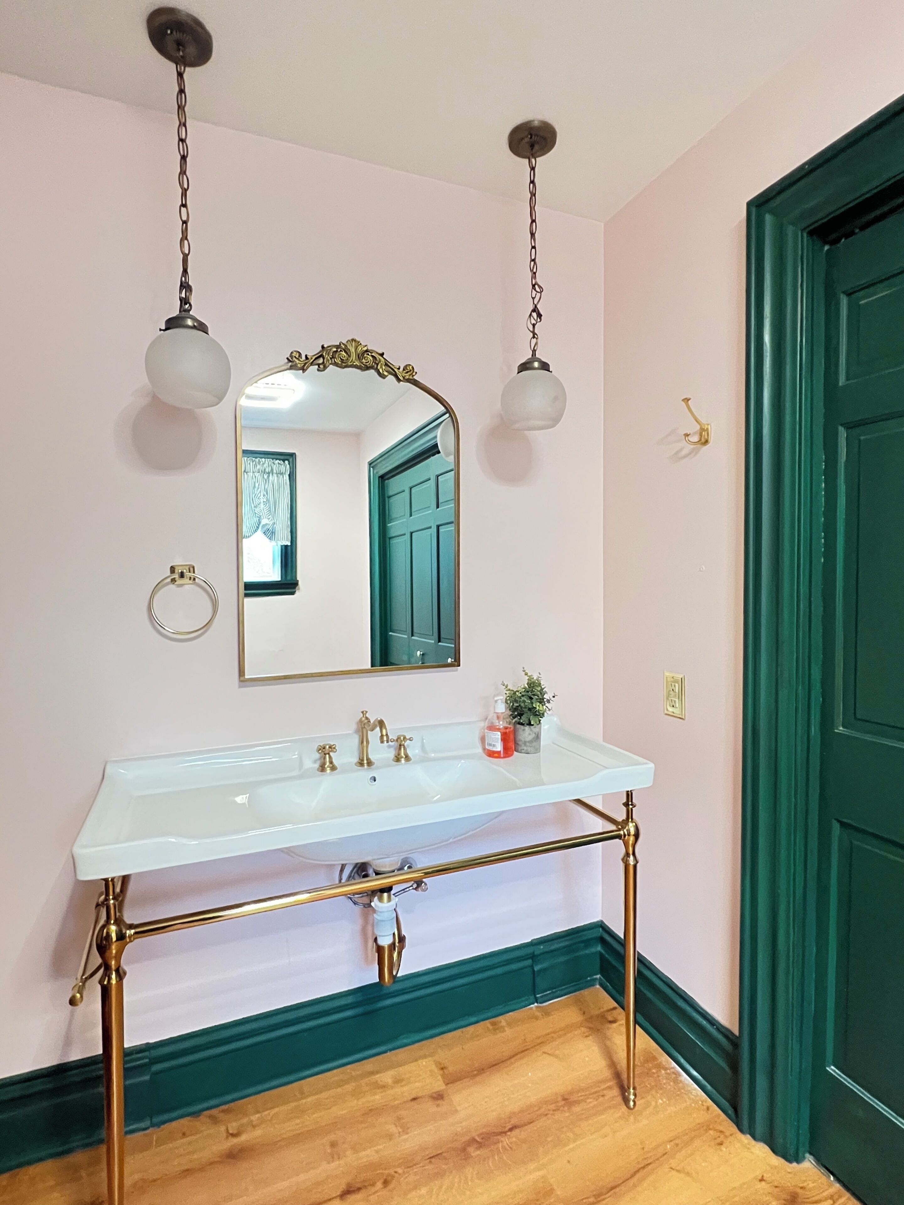 A bathroom with a white sink, gold fixtures, a mirror, and a green door.