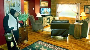 Een gezellige woonkamer met houten plafond, een televisie, een bank, een fauteuil en een decoratief berenbeeld.