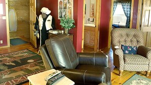 Een woonkamer met een lederen fauteuil, een gestreept armstoel, een houten deur en een spiegel.