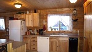 Een kleine keuken met houten kastjes, een koelkast, een vaatwasser en een raam met uitzicht.