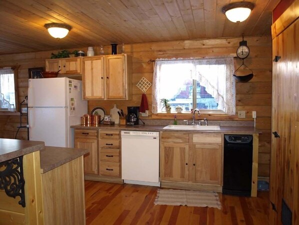 A compact kitchen with wooden cabinets, a refrigerator, a dishwasher, and a window with a view.