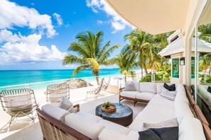 A beachside patio with wicker furniture, a white sofa, and a view of the ocean.