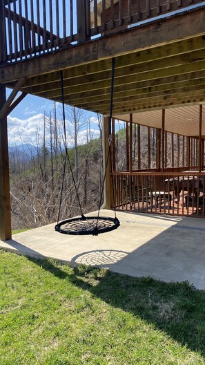 A covered outdoor area with a swing, a patio table, and a view of a mountainous landscape.