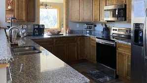 Cocina con armarios de madera, encimeras de granito, electrodomésticos de acero inoxidable y ventana con vista a árboles.