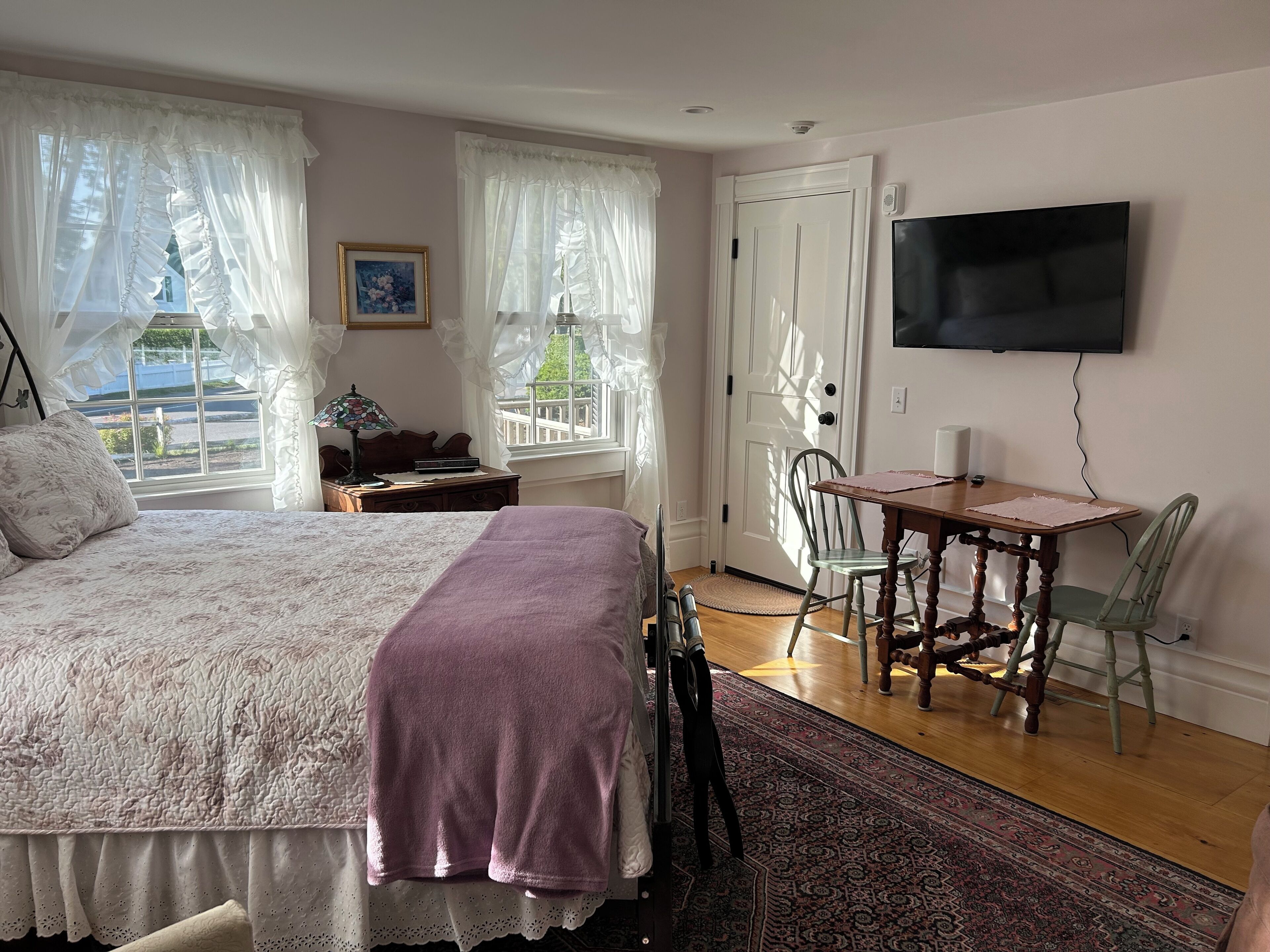 A bedroom with a bed, a desk, a chair, a TV, and a window with curtains.