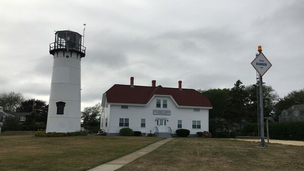 A white lighthouse and a U.S. Coast Guard station building with a red roof, surrounded by a grassy area and trees. - Chatham Village - Adorable Studio Apartment in Antique Home (Chatham)