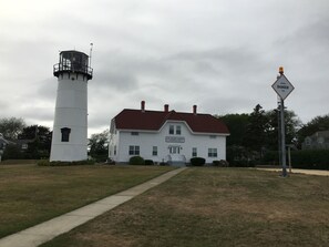 Un faro blanco y un edificio blanco con techo rojo, un letrero para barra de peligro, y un letrero de estación de la Guardia Costera de EE. UU.