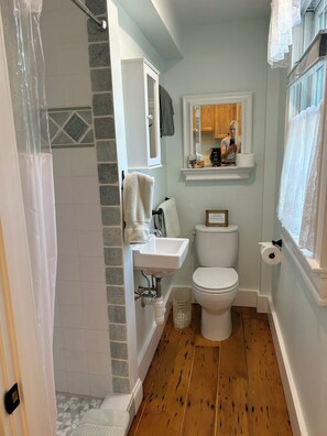 Un baño con ducha, inodoro, lavabo y una ventana con cortinas de encaje.