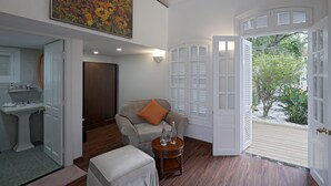 Una habitación con sofá, una mesita redonda con botellas, un cuadro sobre el sofá y una puerta que da a un espacio exterior.