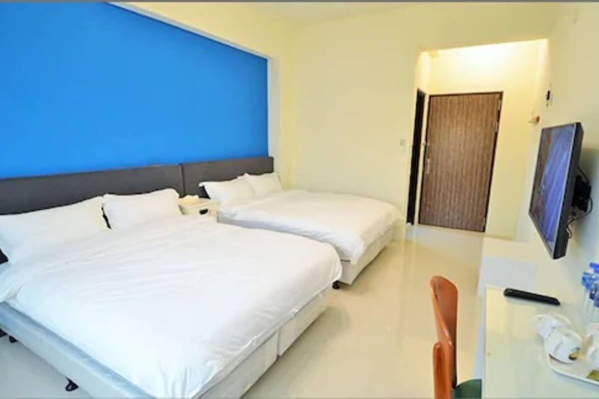 A hotel room with two beds, a desk with a chair, a TV, and a door.