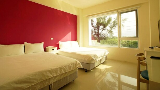 A hotel room with two beds, a red accent wall, a large window with a view, and a desk with a chair. - Kinginn (Taitung)
