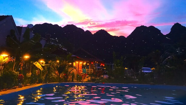 A nighttime view of a resort with a swimming pool reflecting the sky, surrounded by mountains and illuminated buildings. - Lucky Homes (Phong Nha)