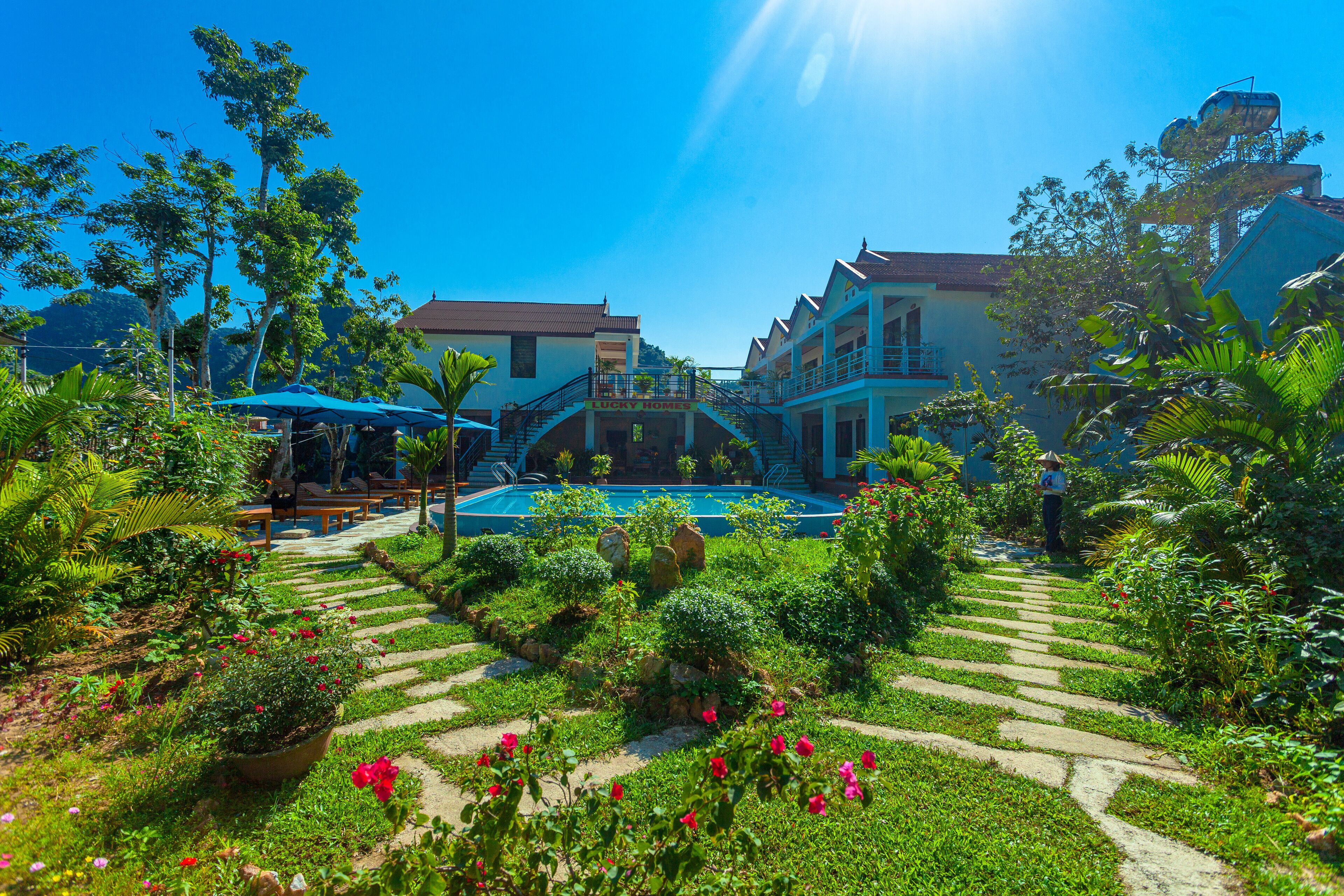 Un hotel con piscina, rodeado de exuberantes jardines y un cielo azul brillante.
