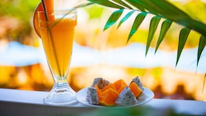 A tall glass of orange juice with a slice of orange and a straw, next to a plate with dragon fruit and mango slices. - Lucky Homes (Phong Nha)