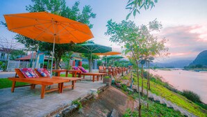 Outdoor seating with umbrellas, a river view, and a stone pathway. - Lucky Homes (Phong Nha)